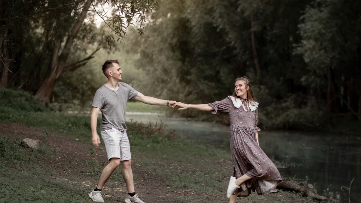 A joyful couple holding hands and walking in a lush green park during the day.